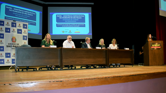 imagem mostra mesa de debates com cinco pessoas sentadas atrás de uma mesa no palco do auditório