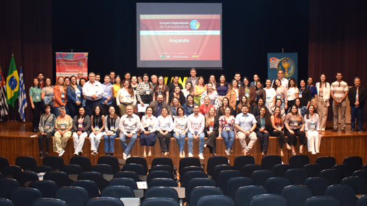 Palco com aproximadamente 50 presentes sentados e de pé, distribuídos pela foto