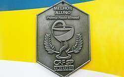 Uma medalha hexagonal de prata escrito melhor aluno e o simbolo do CRF-SP