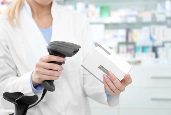 Farmacêutica loira com jaleco branco segura uma caixa de medicamento e um leitor de código de barras