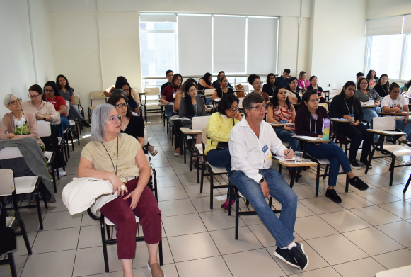 Foto de auditório com público diversificado, composto com pessoas de etnias e faixas etárias diferentes