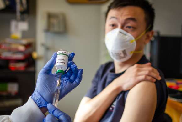 Farmacêutico prepara  seringa para vacinar paciente que aguarda com manda da camiseta levantada