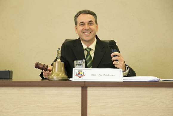 Imagem do vereador Rodrigo Modanez apoiado sobre uma mesa bege.