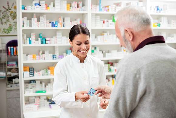 Farmacêutica conversa com idoso em farmácia.