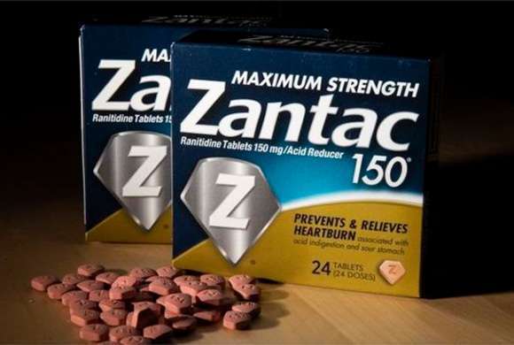 Duas caixas de medicamentos onde lê-se "Zantac" e comprimidos espalhados a sua frente.