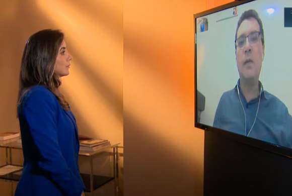 Repórter faz entrevista pela internet olhando para tela com imagem do Dr. Marcos Machado