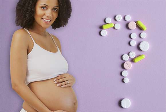Uma mulher grávida acaricia sua barriga. À direita, um ponto de interrogação formado por cápsulas de medicamento