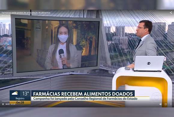 De um lado uma repórter na tela e de outro o apresentador Rodrigo Bocardi durante reportagem sobre a campanha farmácia solidária. Na tela, a inscrição Farmácias recebem alimentos doados 